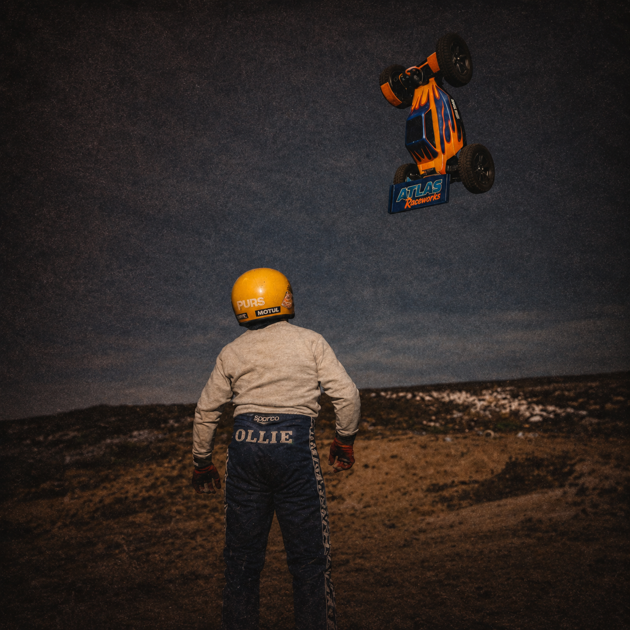 Person in racing suit and helmet observing a remote-controlled car performing a trick in the air.